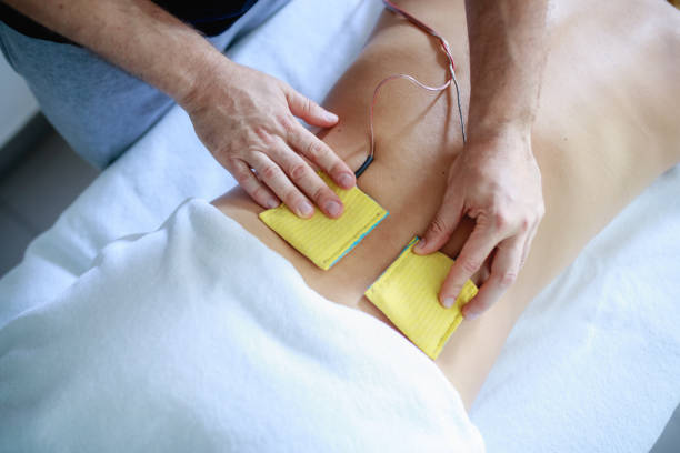 Physiotherapist's hands holding pads down on patient's lower back for electrotherapy stimulation